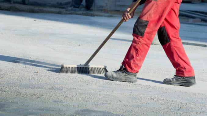Mann in Arbeitsschuhen fegt Straße Mann in Arbeitsschuhen fegt Straße